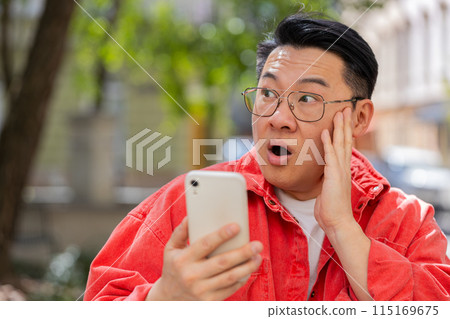 Excited happy Asian mature man use smartphone celebrating win good message news in city street 115169675