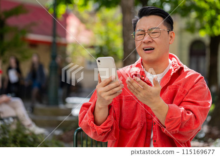 Surprised Asian man use smartphone loses, bad news, fortune loss, fail outdoors in city street Surprised Asian man use smartphone loses, bad news, fortune loss, fail outdoors in city street 115169677