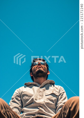 A man wearing sunglasses and a white shirt is sitting on a bench A man wearing sunglasses and a white shirt is sitting on a bench 115171140