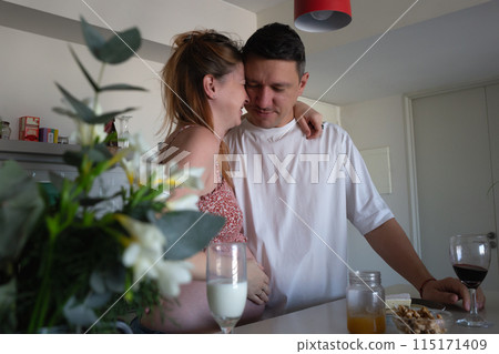 A happy couple in the kitchen, laughing and embracing, as they eagerly anticipate the arrival of their baby 115171409