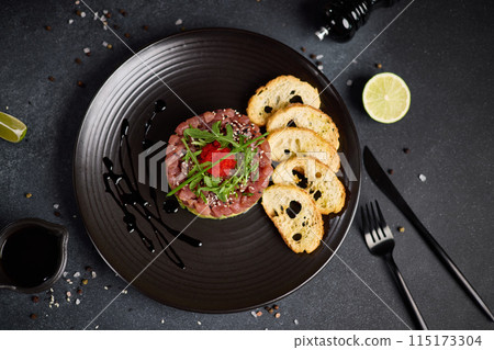 Tuna and avocado tartare on a dark ceramic plate 115173304
