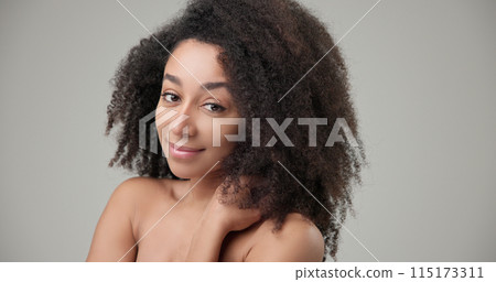 Beauty and Healthcare concept - Beautiful African American woman with curly afro hairstyle hair and clean, healthy skin on gray studio background posing and looking at camera 115173311