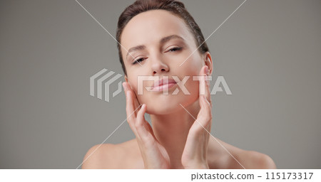 Beauty, health, cosmetics, anti-aging therapy and skin care concept - young beautiful brunette Caucasian woman touching her face skin with her hands, posing and looking at the camera as in a mirror Beauty, health, cosmetics, anti-aging therapy and skin care concept - young beautiful brunette Caucasian woman touching her face skin with her hands, posing and looking at the camera as in a mirror 115173317