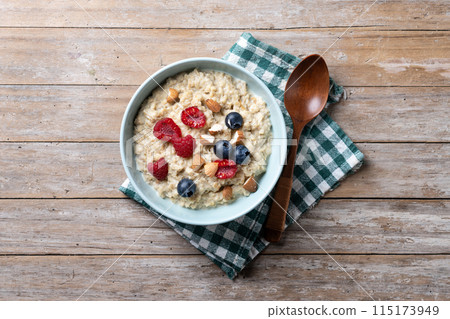 Oatmeal porridge with raspberries, blueberries and almonds in bowl on wooden table 115173949