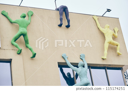 Great deals at the mall. The building is beige in color with an installation in the form of people climbing the wall. The concept of shopping, people are rushing to the sale. High quality photo Great deals at the mall. The building is beige in color with an installation in the form of people climbing the wall. The concept of shopping, people are rushing to the sale. High quality photo 115174251