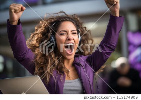 A woman in an office setting raises her fists in victory, clearly elated by a successful moment. A woman in an office setting raises her fists in victory, clearly elated by a successful moment. 115174909