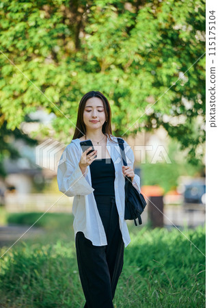 A young woman walking while operating a smartphone A young woman walking while operating a smartphone 115175104