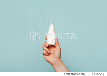 A hand holding a white spray bottle against a light blue background A hand holding a white spray bottle against a light blue background 115176547