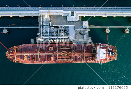 Aerial top down view of a large oil tanker docked at a pier in the port in process of loading. Aerial top down view of a large oil tanker docked at a pier in the port in process of loading. 115176635