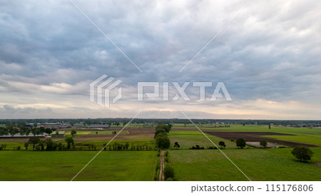 Aerial view of expansive green fields under a cloudy sky, showcasing a rural landscape Aerial view of expansive green fields under a cloudy sky, showcasing a rural landscape 115176806