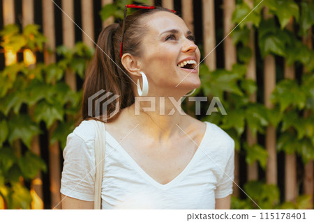happy young 40 years old woman in white shirt near wooden wall 115178401