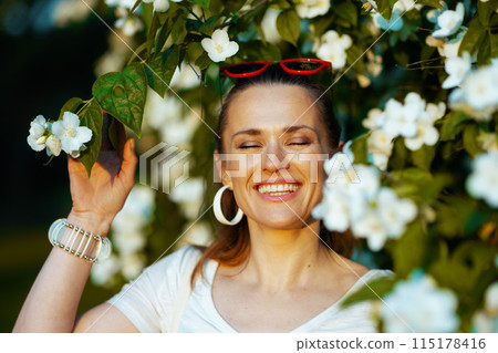 happy modern woman in white shirt near flowering tree 115178416