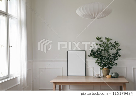 Elegant Scandinavian living room interior. Black thin frame poster, picture frame mockup on office table near window. Green tree branches in vase, pumpkins, cup of coffee. Linen lamp shade. Home decor Elegant Scandinavian living room interior. Black thin frame poster, picture frame mockup on office table near window. Green tree branches in vase, pumpkins, cup of coffee. Linen lamp shade. Home decor 115179484