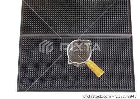 Measuring cup with wooden handle on bar mat over white background. Measuring cup with wooden handle on bar mat over white background. 115179945