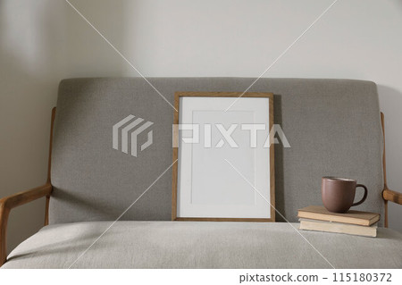 Elegant minimal Scandinavian interior. Blank wooden picture frame mockup. Cup of coffee on pile of old books. Midcentury linen sofa. White wall background. Home office concept. Cozy still life. 115180372