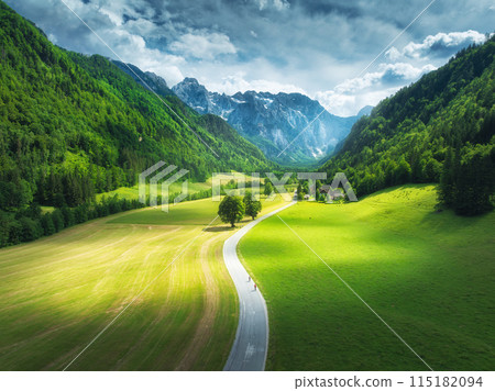 Aerial view of road in mountains, green meadows, trees at sunset Aerial view of road in mountains, green meadows, trees at sunset 115182094