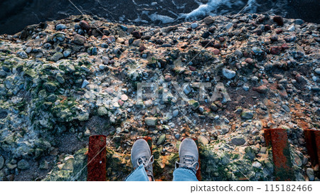 A person is standing on a ledge with their feet on a railing 115182466