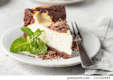 Piece of homemade chocolate cheesecake topped with chocolate chips mint leave on a plate close up on white textured background Piece of homemade chocolate cheesecake topped with chocolate chips mint leave on a plate close up on white textured background 115182684
