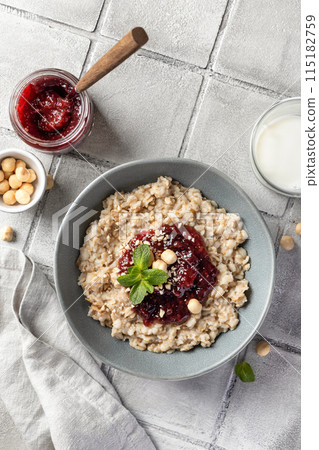 Oatmeal porridge with raspberry jam and nuts in gray bowl on gray tile background, top view. Healthy diet breakfast Oatmeal porridge with raspberry jam and nuts in gray bowl on gray tile background, top view. Healthy diet breakfast 115182759