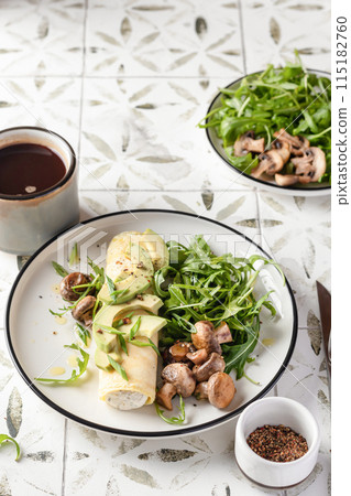 French rolled omelette stuffed with cream cheese with avocado, aragula and mushrooms for breakfast on white plate printed tile background, top view 115182760