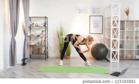 Flexibility training. Internet workout. Body stretch exercise. Video lesson. Fit woman activewear doing sport watching laptop at home interior. 115183881