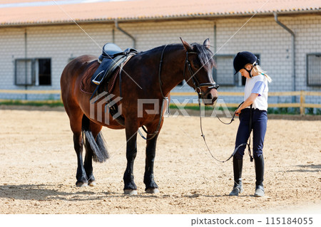 Horse riding school. Little children girls at group training equestrian lessons at outdoors ranch horse riding yard. Cute little beginner blond girl kid near beautiful brown horse Horse riding school. Little children girls at group training equestrian lessons at outdoors ranch horse riding yard. Cute little beginner blond girl kid near beautiful brown horse 115184055