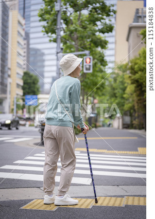 Back view of a senior woman walking down the street with a cane 115184838