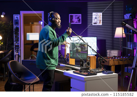 Talented composer artist does a recording session for his acoustic tunes, performing on microphone in home studio. Confident singer working on producing new soundtracks for an album. 115185582