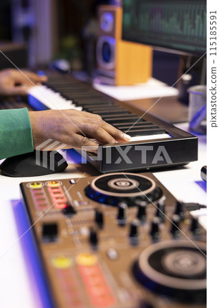 Songwriter playing midi controller synthesizer to record acoustics notes over old audio recordings, editing songs in home studio. Producer working with stereo gear to mix and master tunes. Close up. Songwriter playing midi controller synthesizer to record acoustics notes over old audio recordings, editing songs in home studio. Producer working with stereo gear to mix and master tunes. Close up. 115185591