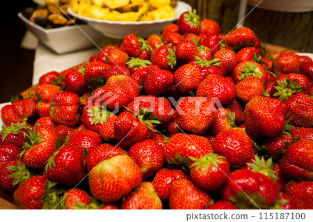 Fresh ripe strawberries neatly piled with an assortment of fruits in the background 115187100