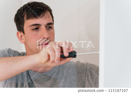 Close-up of a young professional carpenter using a hand-held screwdriver Close-up of a young professional carpenter using a hand-held screwdriver 115187107