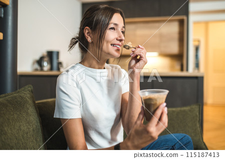 Cute young woman eating dessert from the glass and looking enjoyed 115187413