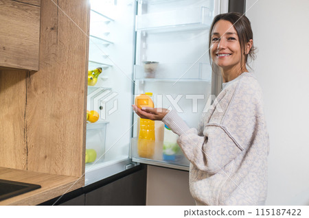 Smiling contented woman standing near the fridge in the kitchen 115187422