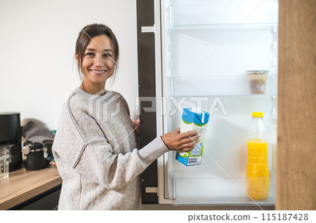 Young dark-haired woman opening fridge and taking a bottle of milk 115187428