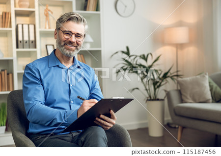 Happy male psychologist with clipboard looking at camera and smiling 115187456