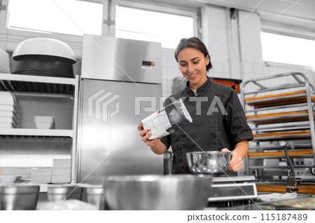 Woman in uniform kneading dough in kitchen preparing pastry in kitchen Woman in uniform kneading dough in kitchen preparing pastry in kitchen 115187489