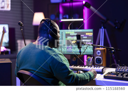 Young artist producer writing lyrics and musical notes to create new tracks in home studio, thinking about acoustics and lines for a modern cool soundtrack. Songwriter composing tracks with gear. Young artist producer writing lyrics and musical notes to create new tracks in home studio, thinking about acoustics and lines for a modern cool soundtrack. Songwriter composing tracks with gear. 115188560
