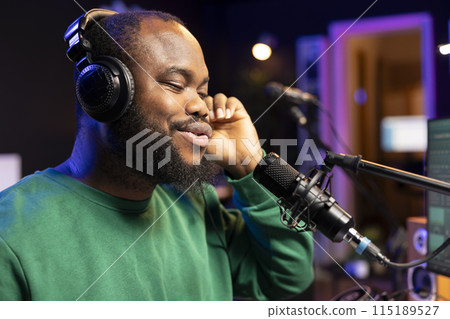 Confident songwriter performing a tune on microphone in home studio, recording his song and editing in post production. Performer artist singing aloud and using stereo equipment. Close up. Confident songwriter performing a tune on microphone in home studio, recording his song and editing in post production. Performer artist singing aloud and using stereo equipment. Close up. 115189527