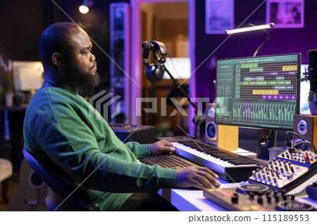 African american artist composing a new soundtrack for a project, using professional production software in his home studio. Skilled creative singer producing music and adding sound effects. 115189553