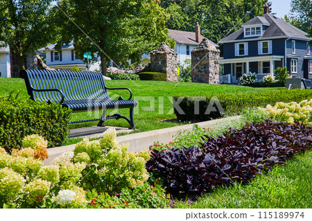 Black bench with variety of plants and stone gateway to park and houses in background Black bench with variety of plants and stone gateway to park and houses in background 115189974