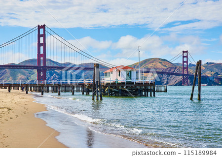 Beach with waves and pier with small shack with Golden Gate Bridge behind it Beach with waves and pier with small shack with Golden Gate Bridge behind it 115189984