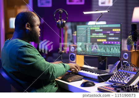 Sound engineer recording piano notes with DAW software in his home studio, working at night on producing new music with electronic tools. Musician composing tunes on midi controller. 115190073