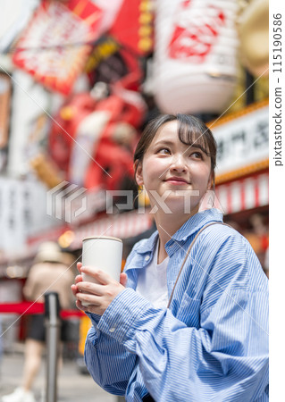 Young and pretty woman holding a drink in a busy urban area | Osaka tourism image | Dotonbori shopping street, Osaka city, Osaka prefecture Young and pretty woman holding a drink in a busy urban area | Osaka tourism image | Dotonbori shopping street, Osaka city, Osaka prefecture 115190586