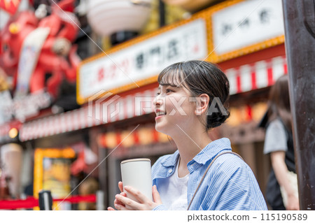 Young and pretty woman holding a drink in a busy urban area | Osaka tourism image | Dotonbori shopping street, Osaka city, Osaka prefecture 115190589