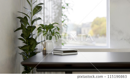 A table near the window featuring a reed diffuser, books, and plants in a minimalist white room. A table near the window featuring a reed diffuser, books, and plants in a minimalist white room. 115190863