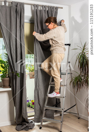 A woman hangs curtains 115191283