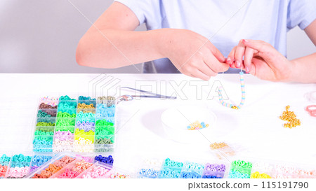 Delicate fingers of a young girl navigate through a treasure trove of bright, multicolored beads, each compartment revealing a new hue to choose from. 115191790