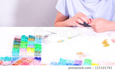 Delicate fingers of a young girl navigate through a treasure trove of bright, multicolored beads, each compartment revealing a new hue to choose from. 115191791