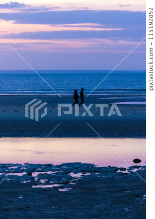 Silhouette of a couple enjoying a peaceful walk on a serene beach during a beautiful purple sunset Silhouette of a couple enjoying a peaceful walk on a serene beach during a beautiful purple sunset 115192052