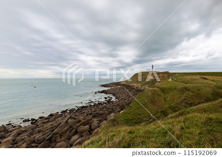 Marvel at the breathtaking rocky coastline with a lighthouse under a moody overcast sky 115192069